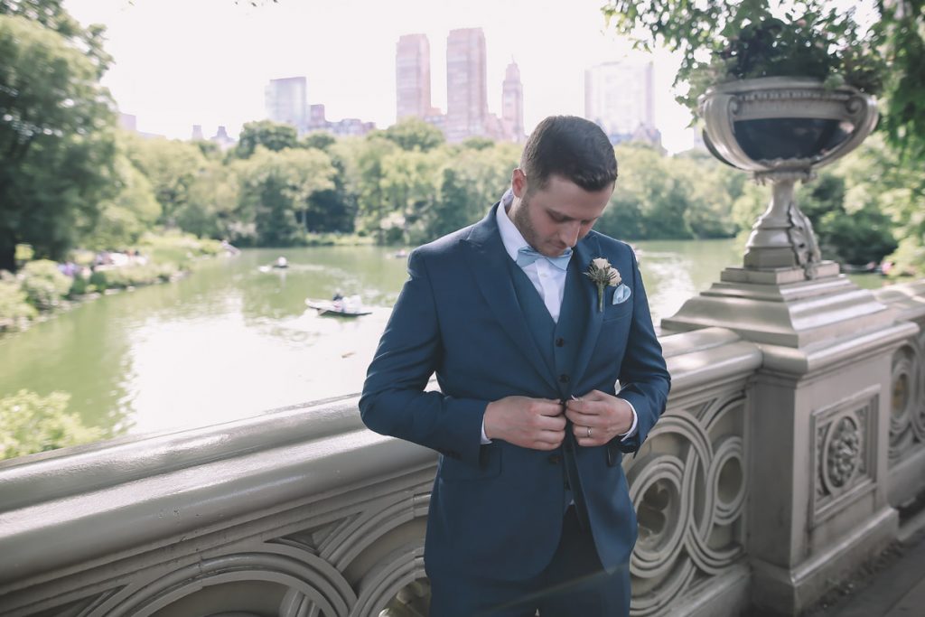 summer wedding central park on bow bridge brazilian groom buttoning up his jacket