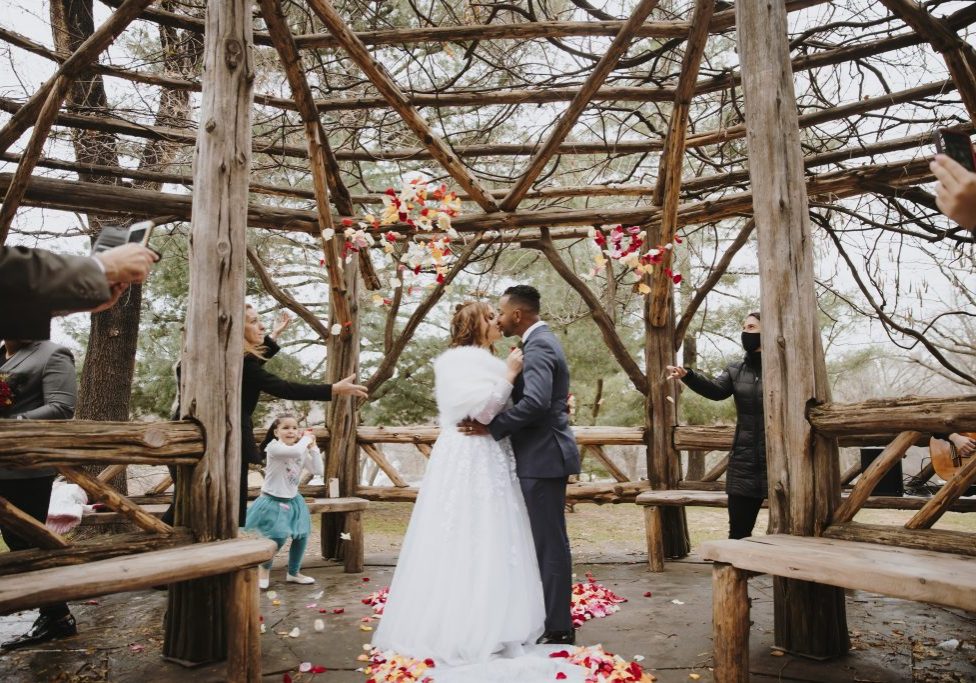 Family throws rose petals at kissing couple in Cop Cot, Central Park wedding